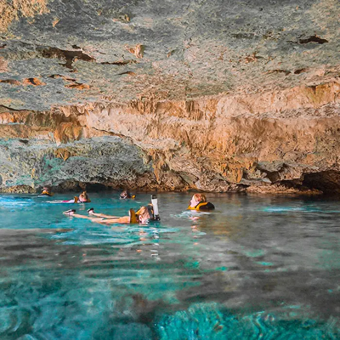 Group swimming inside a stunning cenote with crystal-clear water and rock formations during the Adventure Snorkeling Tour