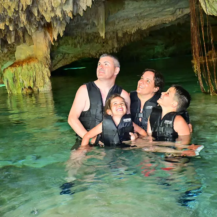 Family wearing life jackets exploring a beautiful cave cenote, one of the unique stops of the snorkeling tour