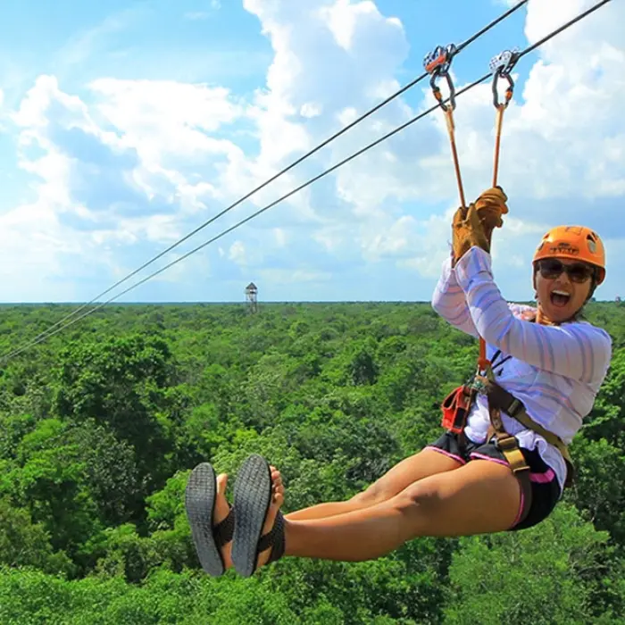 Woman smiling mid-zipline above the jungle treetops, enjoying the thrill of the Mayan Adventure Tour
