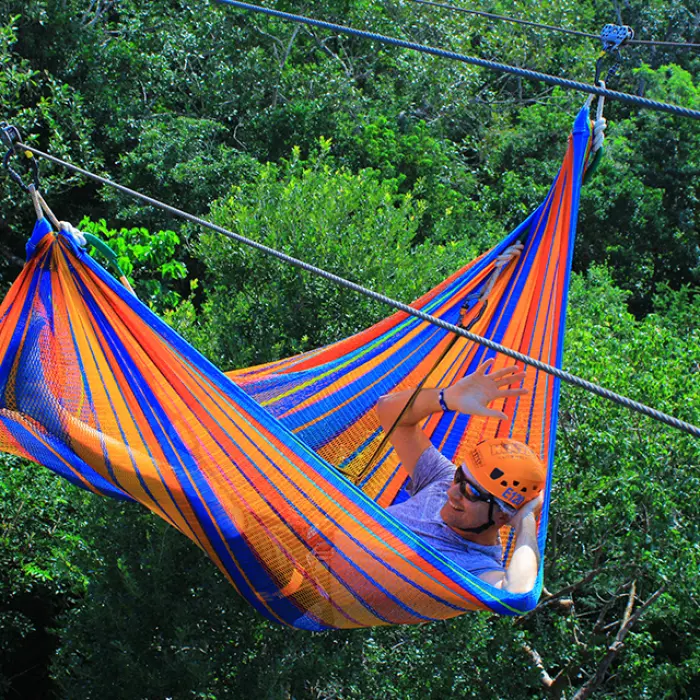 Woman relaxing mid-air on a colorful hammock zipline surrounded by trees