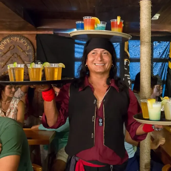 Captain Hook Cancun bar, showing a server in pirate attire carrying trays of colorful drinks