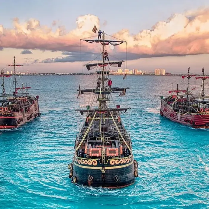 Captain Hook Cancun fleet: Aerial view of three illuminated pirate ships sailing on the turquoise waters near Cancun at sunset
