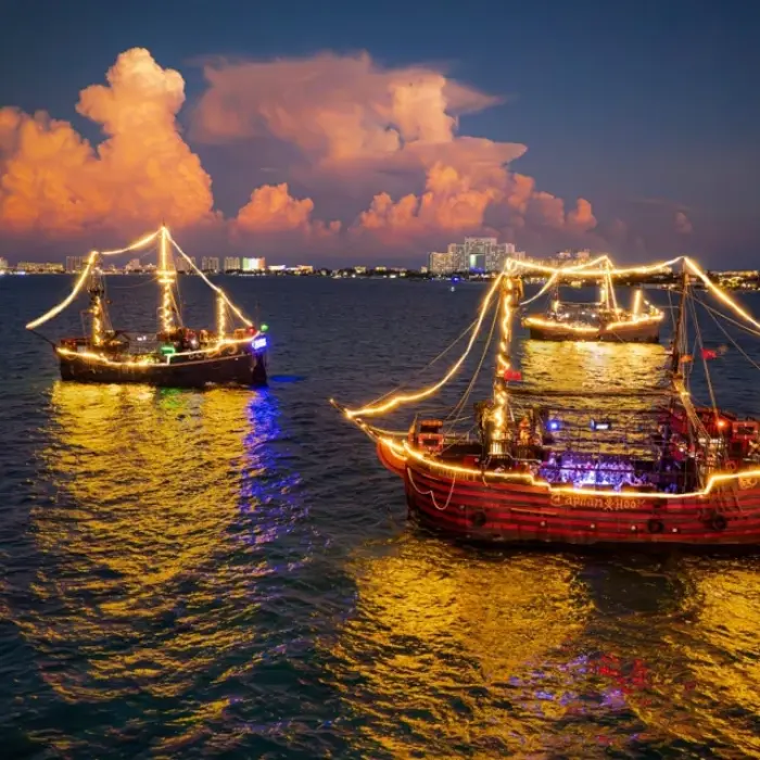 Captain Hook Cancun illuminated pirate ships, sailing on the water at night with city lights in the background