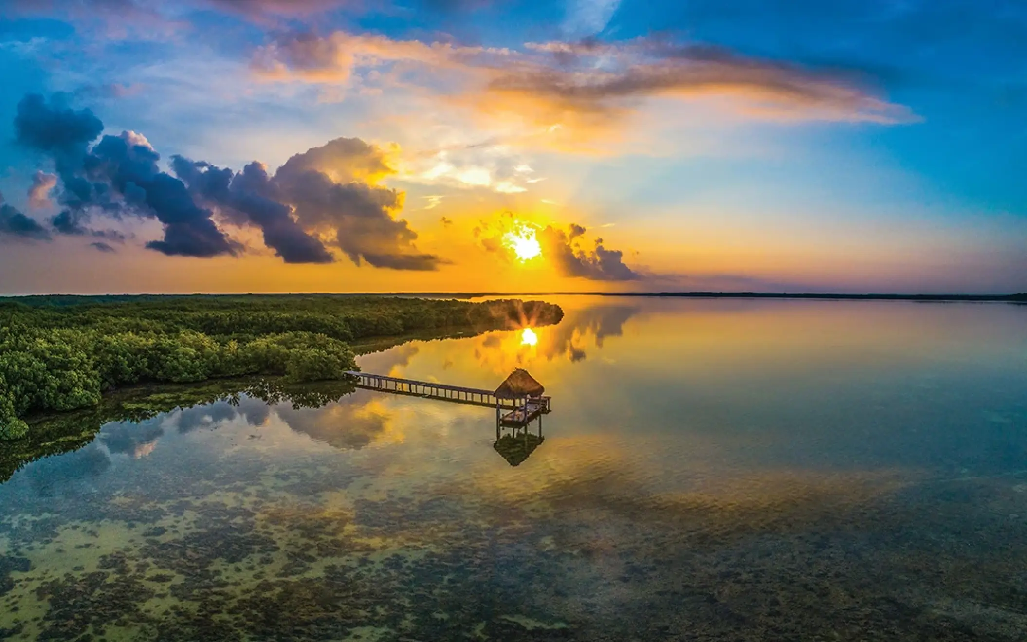 A gorgeous sunset over the Rio Lagartos biosphere reserve, with a rustic dock stretching into the calm water surrounded by lush mangroves.