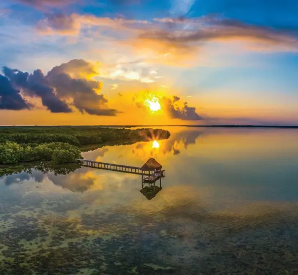 A gorgeous sunset over the Rio Lagartos biosphere reserve, with a rustic dock stretching into the calm water surrounded by lush mangroves.