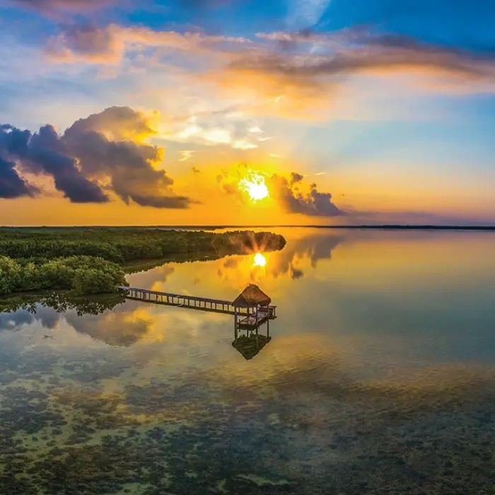 A gorgeous sunset over the Rio Lagartos biosphere reserve, with a rustic dock stretching into the calm water surrounded by lush mangroves.