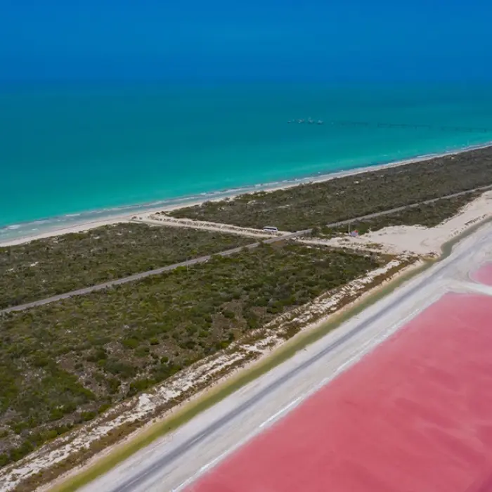 A stunning drone shot showing the contrast between the vibrant pink lakes of Las Coloradas and the brilliant turquoise of the nearby ocean.