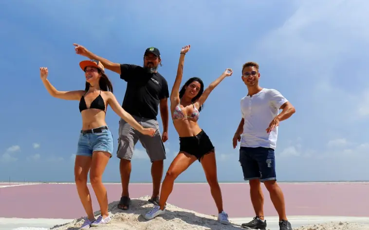 A group of friends having fun and posing for a photo on the salt mounds with the incredible pink lakes of Las Coloradas behind them.