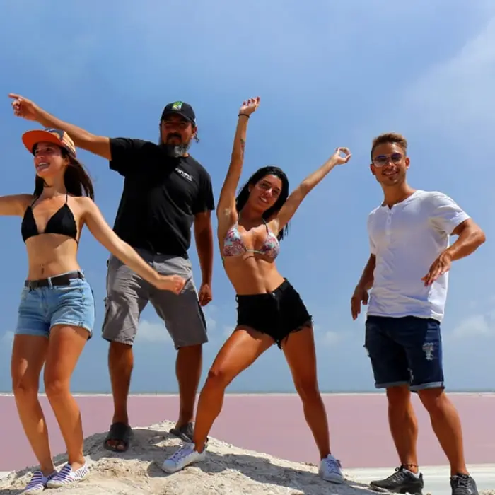 A group of friends having fun and posing for a photo on the salt mounds with the incredible pink lakes of Las Coloradas behind them.
