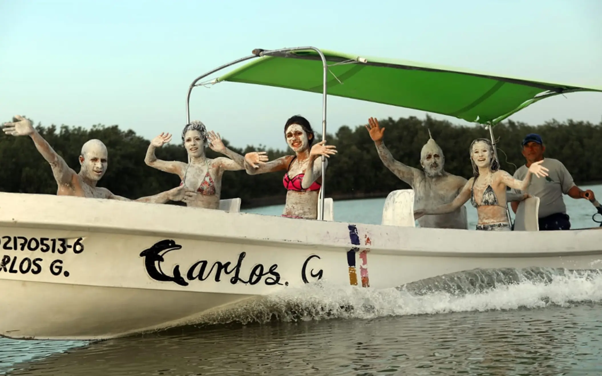 A fun-loving group on a boat in Rio Lagartos, covered in nourishing mineral clay after enjoying a traditional Mayan bath experience.