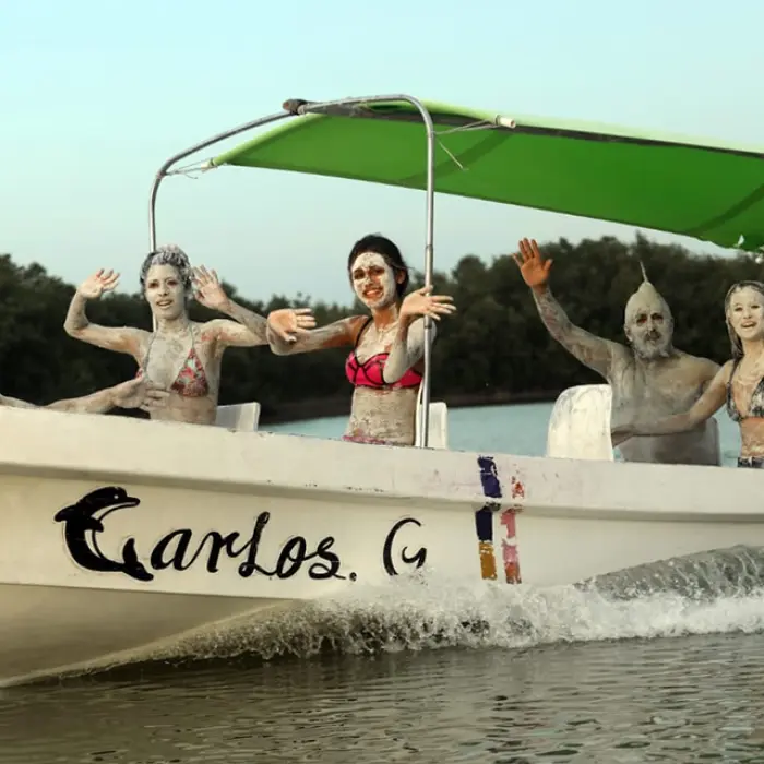 A fun-loving group on a boat in Rio Lagartos, covered in nourishing mineral clay after enjoying a traditional Mayan bath experience.