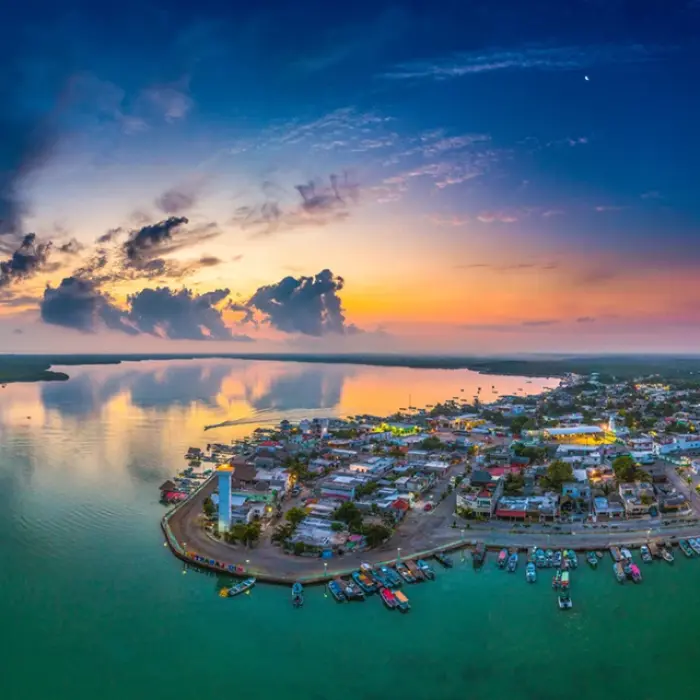 A stunning panoramic sunset view of the Rio Lagartos fishing village, with colorful boats docked along the calm, expansive lagoon.