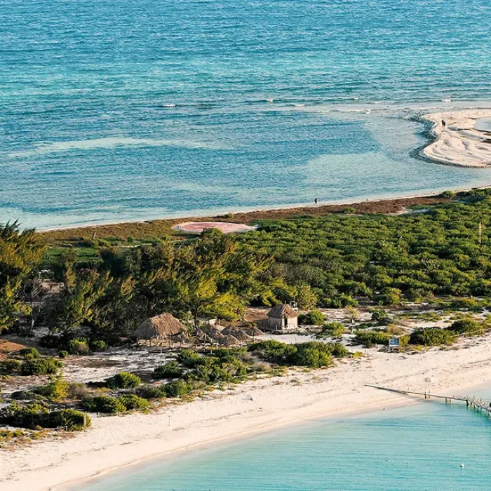 A beautiful aerial view of the Rio Lagartos coastline, featuring a classic red-and-white striped lighthouse, sandy beaches, and turquoise water.