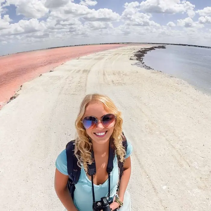 A happy female traveler takes a selfie on the salt flats dividing the famous pink lake from the lagoon at Las Coloradas, Mexico.