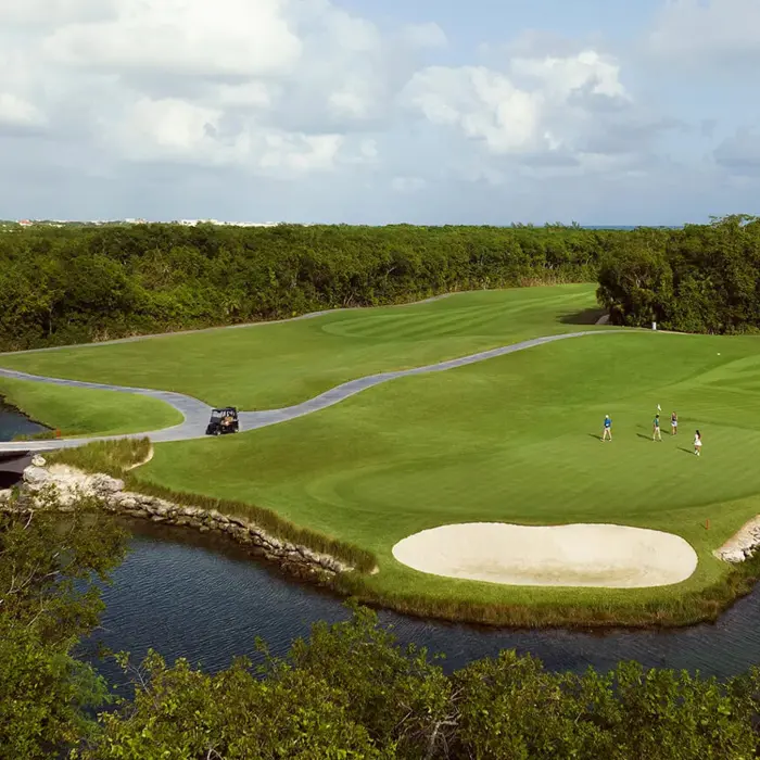 An aerial shot of a stunning golf hole perfectly integrated into the natural lagoons and dense mangrove forests of the Riviera Maya.