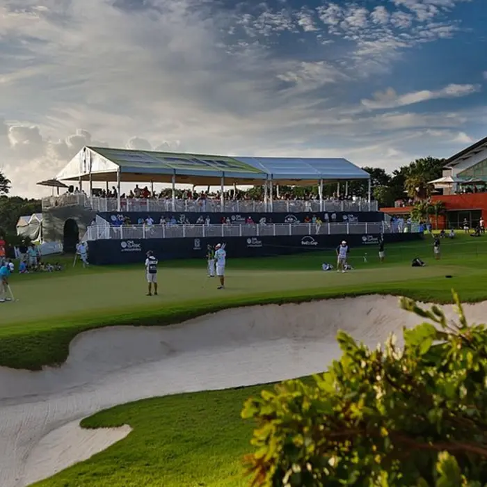 Golfers playing out of a sand bunker near the luxury clubhouse hospitality tents during a championship round at El Camaleón.