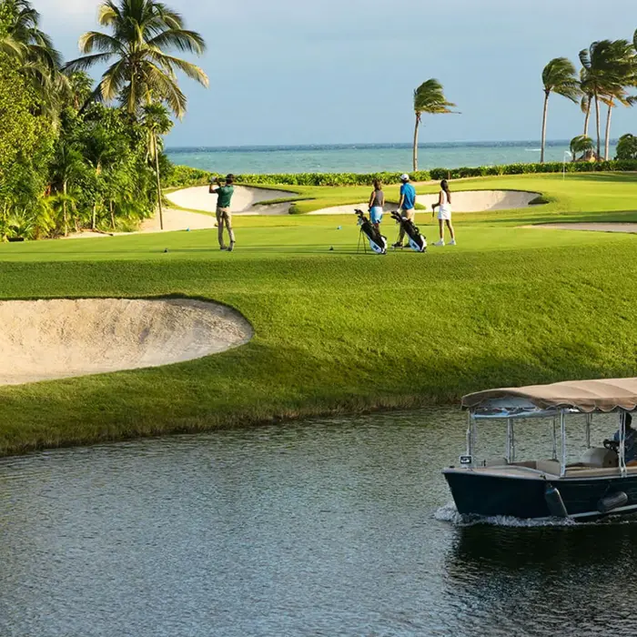 A scenic golf hole surrounded by palm trees with a premium eco-boat cruising through the freshwater canals of Mayakoba.