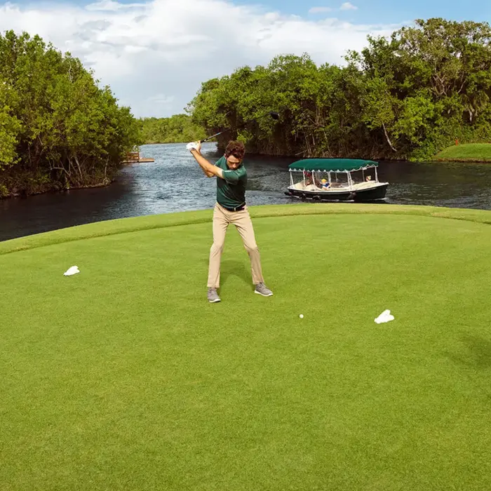 A golfer swings near the water's edge while a guided eco-boat passes by on the canal at the luxury El Camaleón golf course.