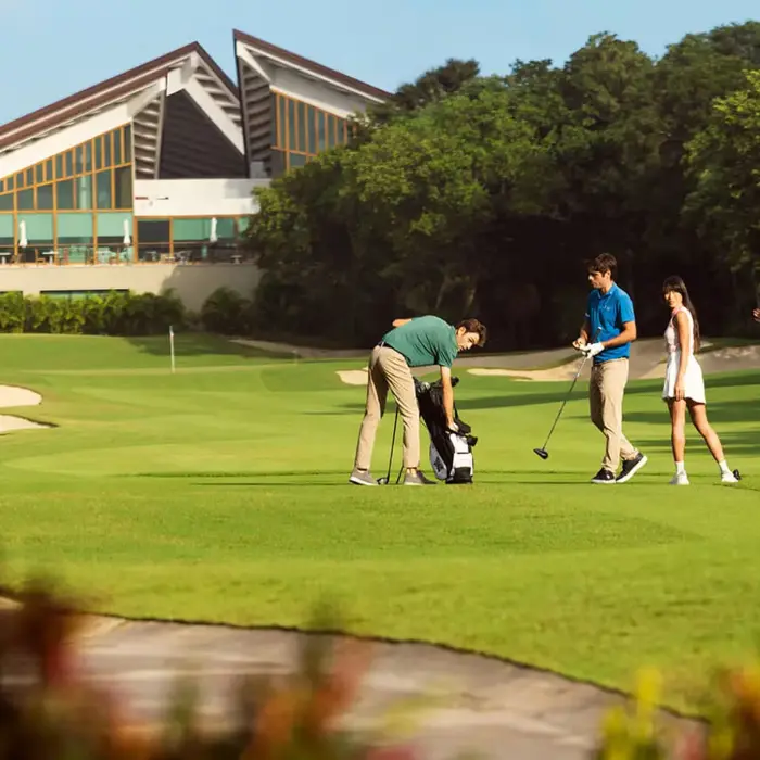 Golfers pull clubs from their bags on the pristine fairway, with the stunning architecture of the El Camaleón luxury clubhouse in the background.