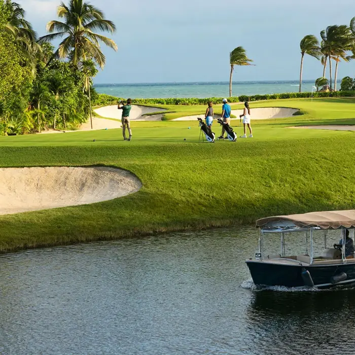 Golfers play on a pristine green surrounded by palm trees while a premium eco-boat glides through the freshwater canal at Mayakoba.
