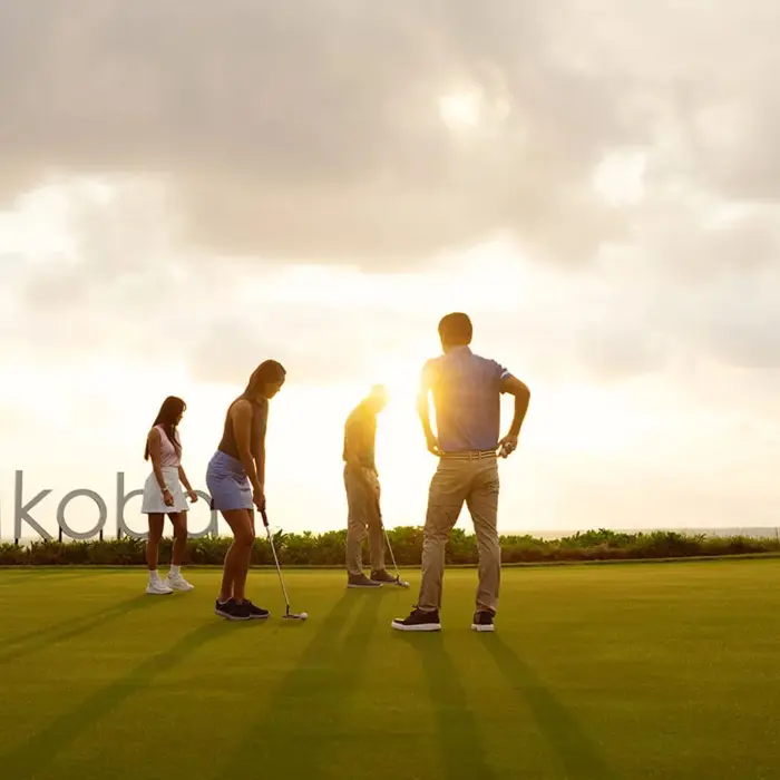 A group of golfers enjoy a spectacular golden hour sunset on the green, right next to the iconic Mayakoba sign.