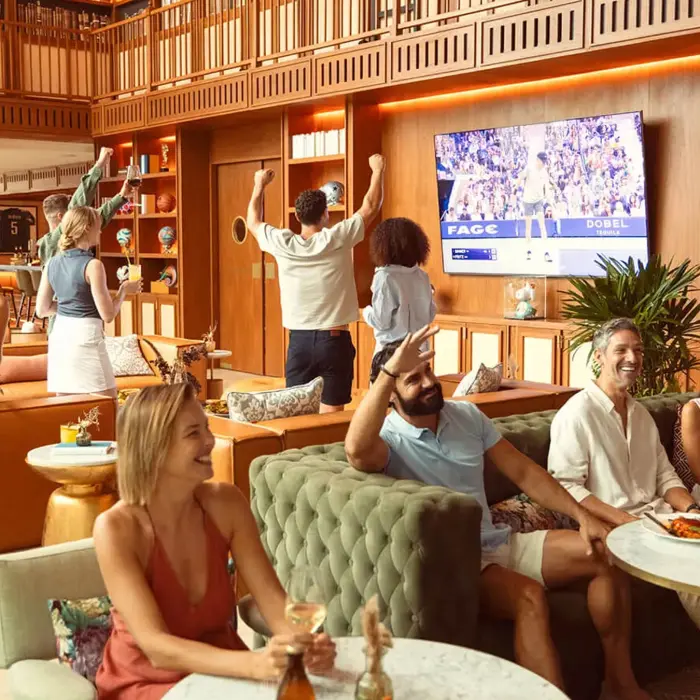 Happy guests celebrate and watch a tournament on TV inside the luxurious, wood-paneled clubhouse bar at El Camaleón Mayakoba.