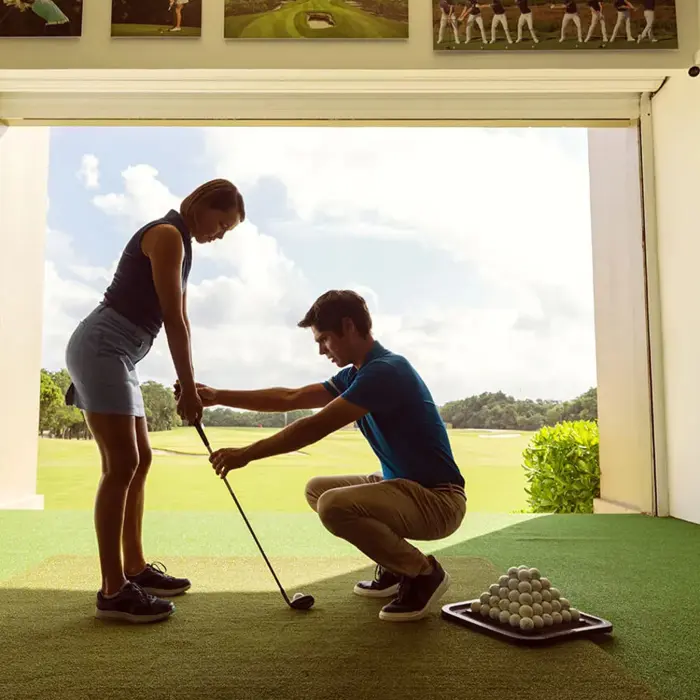A professional golf instructor helps a guest with her stance at the premium indoor-outdoor practice hitting bays in Mayakoba.