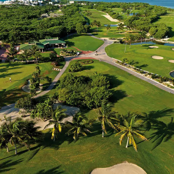 Aerial view of the Gran Coyote Golf Club clubhouse, practice facilities, and palm tree-lined fairways in Playa del Carmen.