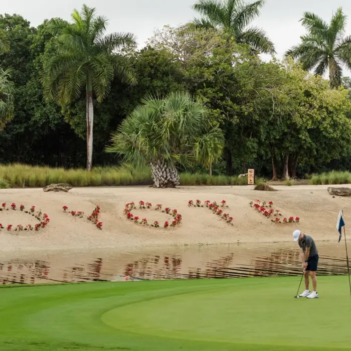A golfer putts on the green near a lake featuring the word Coyote spelled in beautiful red flowers.