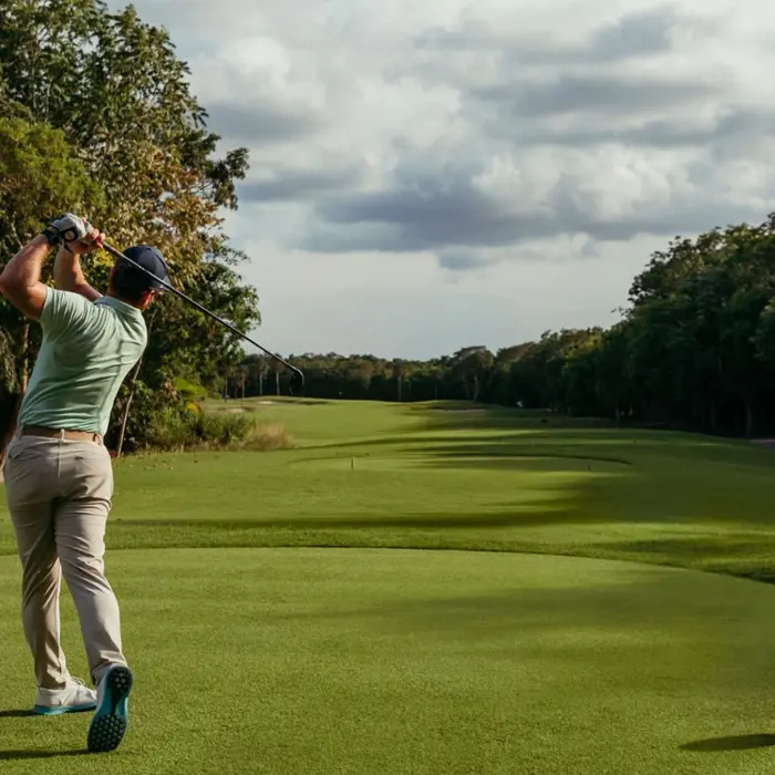 A golfer tees off down a wide, beautifully manicured fairway surrounded by jungle at Gran Coyote.