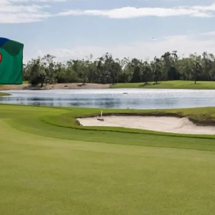A close-up of the Gran Coyote flag on a pristine green with a challenging sand bunker and beautiful lake in the background.