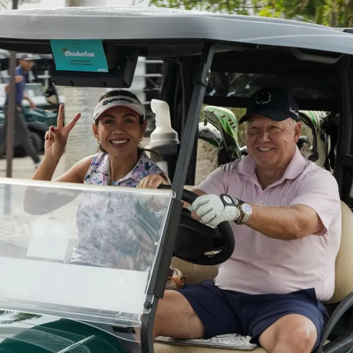 A smiling couple gives a peace sign from their golf cart while enjoying a fun day at Gran Coyote.