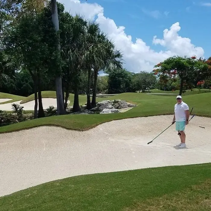 A happy golfer standing in a sand bunker after making a shot at the tropical Hard Rock championship golf course.