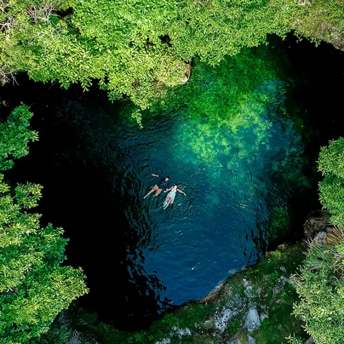Cenote near Playa del Carmen: Aerial view of people swimming in a clear, dark cenote surrounded by lush green trees