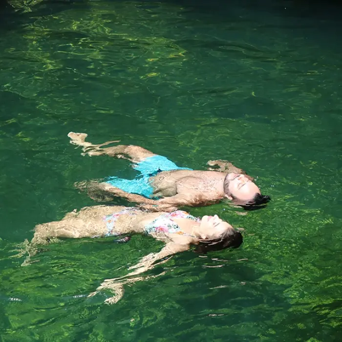 Cenote swim Playa del Carmen: Couple relaxing while floating on their backs in the clear, greenish water of a cenote