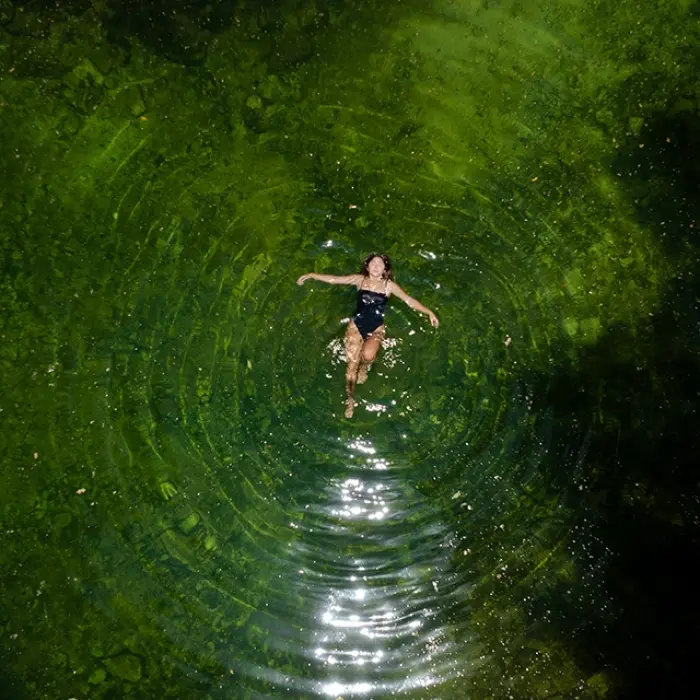 Cenote relaxation Playa del Carmen: Aerial view of a woman floating peacefully in the clear, green water of a cenote, creating ripples