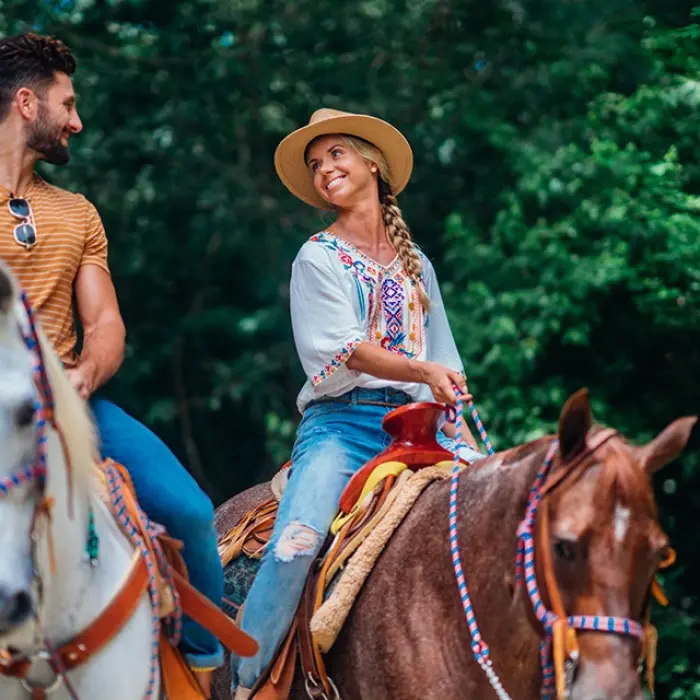 Romantic horseback ride Playa del Carmen: Smiling couple riding horses through a lush green area, enjoying their tour