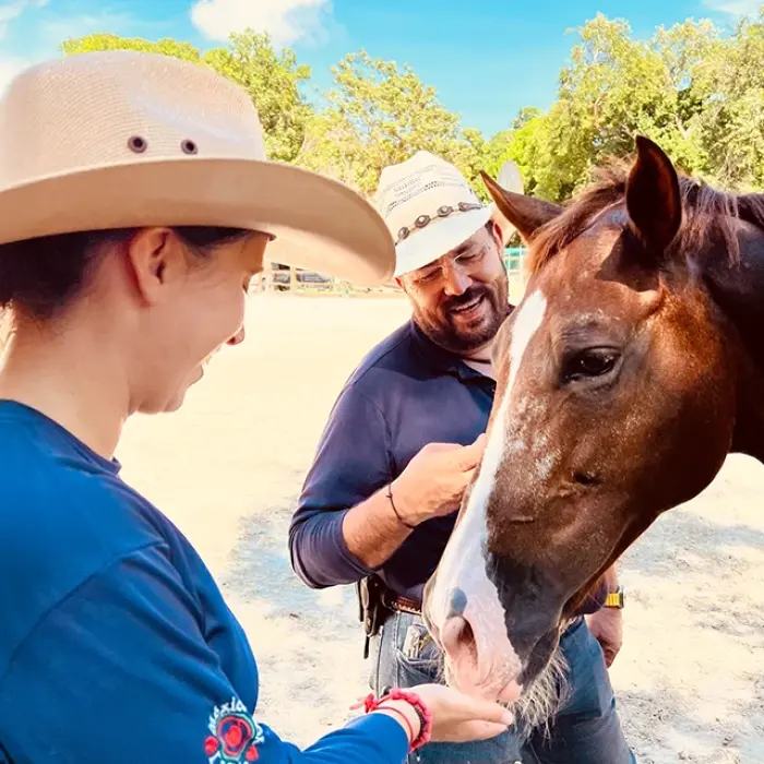 Woman in a cowboy hat interacting with a dark horse at a ranch in Playa del Carmen. Friendly encounter