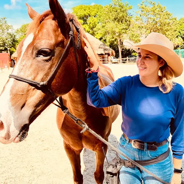 Woman in a cowboy hat leading a brown horse at a ranch in Playa del Carmen. Guiding the way