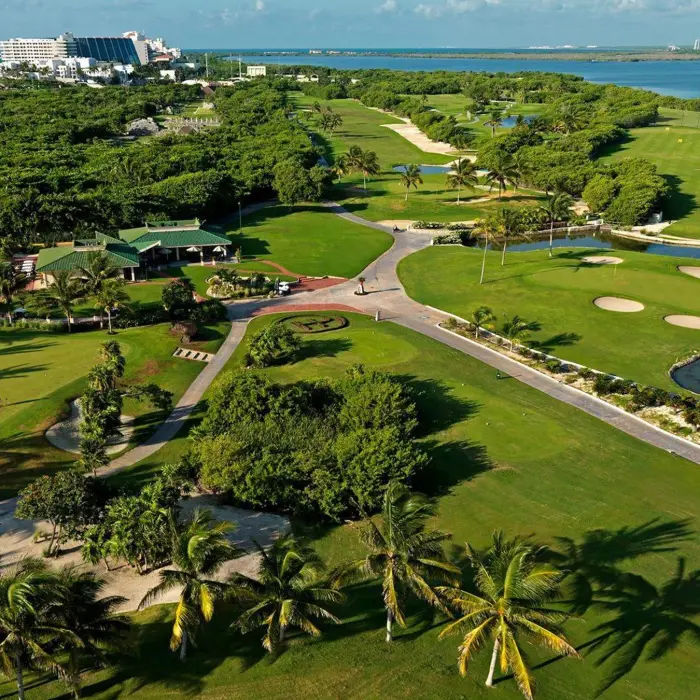 A sweeping aerial view of the Iberostar Golf Club clubhouse, practice greens, water hazards, and the nearby Caribbean coastline