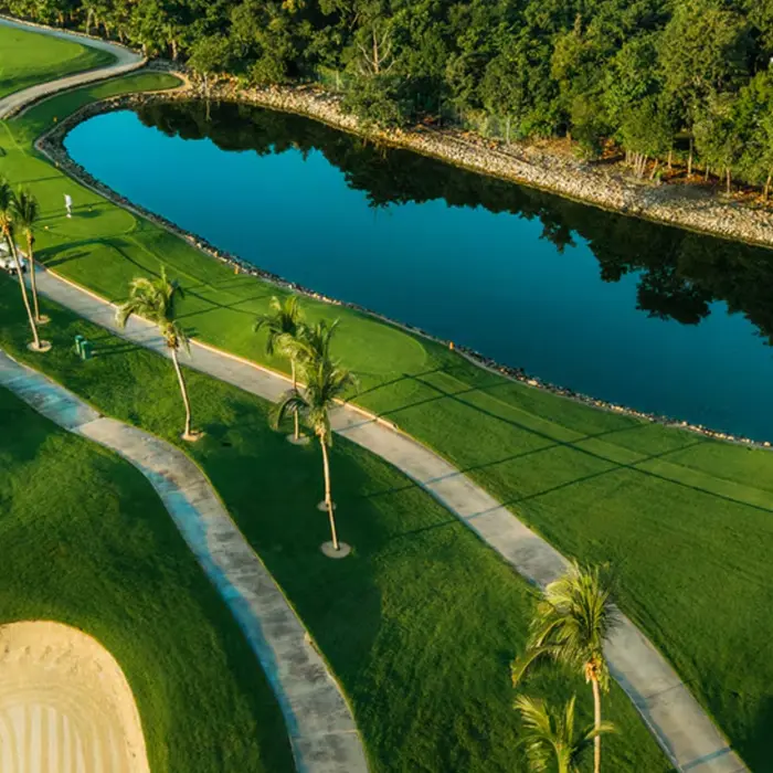 An aerial view of a lush green fairway curving around a pristine blue lake at the P.B. Dye-designed Iberostar Golf Club Playa Paraíso.