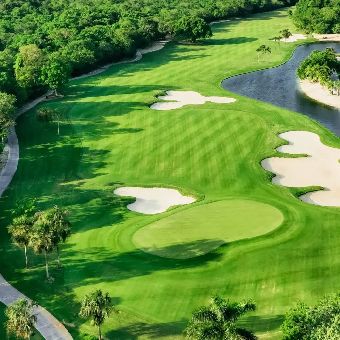Aerial view of a creatively designed golf hole featuring large sand bunkers, a peaceful lake, and surrounding lush jungle