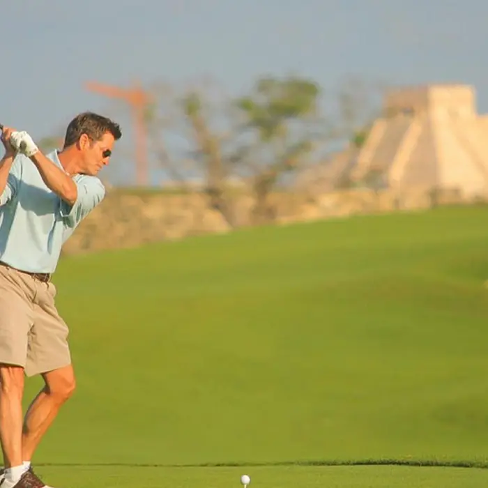 A golfer takes a powerful swing on the fairway with a stunning Mayan pyramid replica in the background at Iberostar