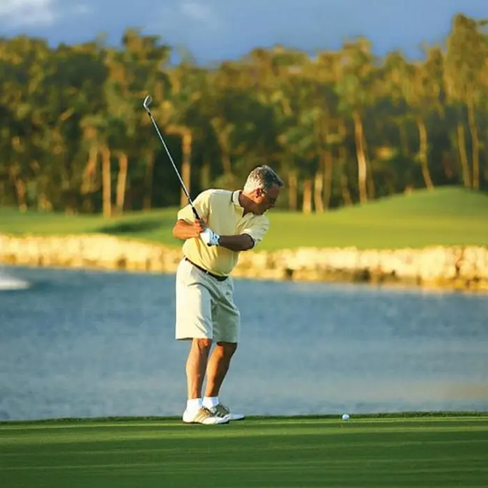 A golfer takes a swing near a scenic water hazard with a beautiful fountain at the tropical Iberostar Golf Club in Riviera Maya.