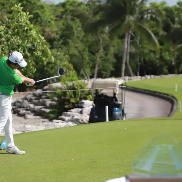 A golfer tees off down a pristine fairway lined with tropical palm trees and natural rock formations at Iberostar