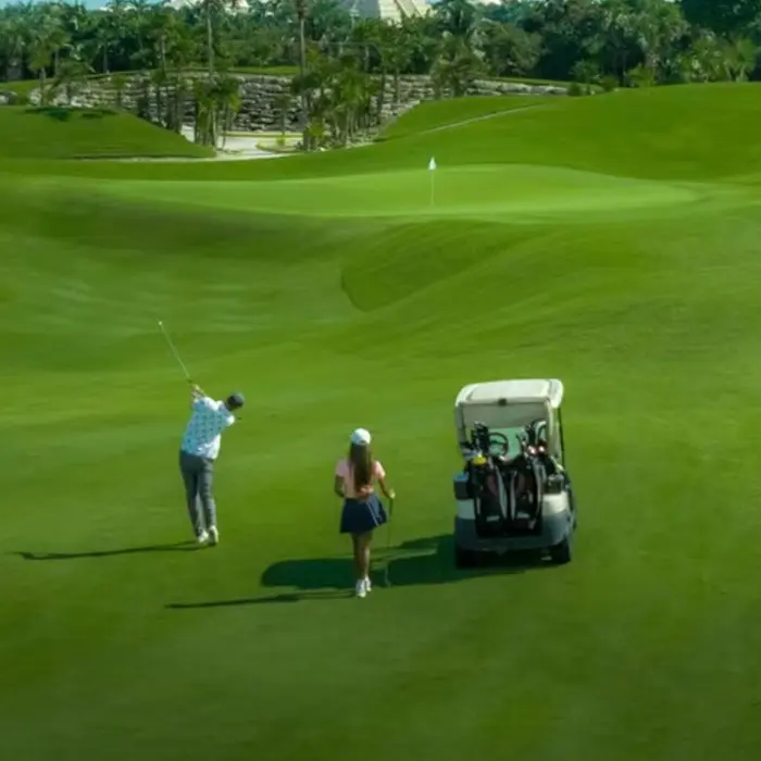 A golfer tees off while his partner watches near their golf cart on a beautifully maintained fairway at Iberostar Playa Paraíso.