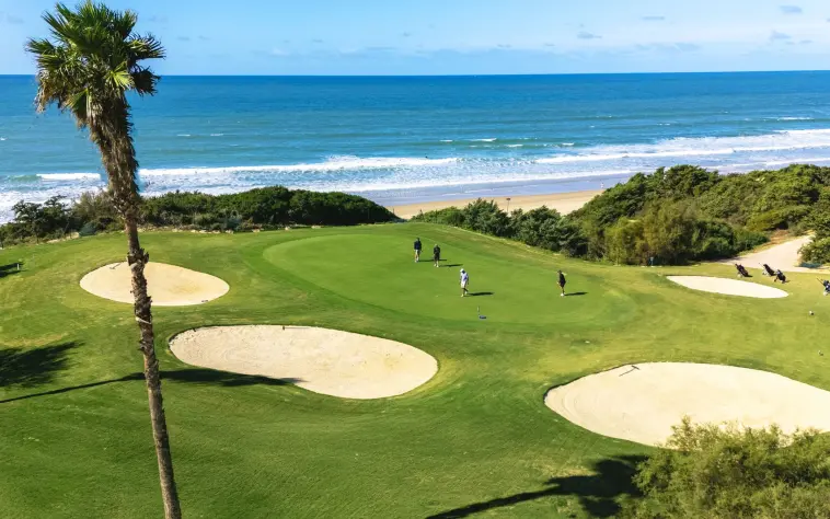Golfers putt on a beautiful oceanfront green bordered by sand bunkers and stunning views of the Caribbean Sea.