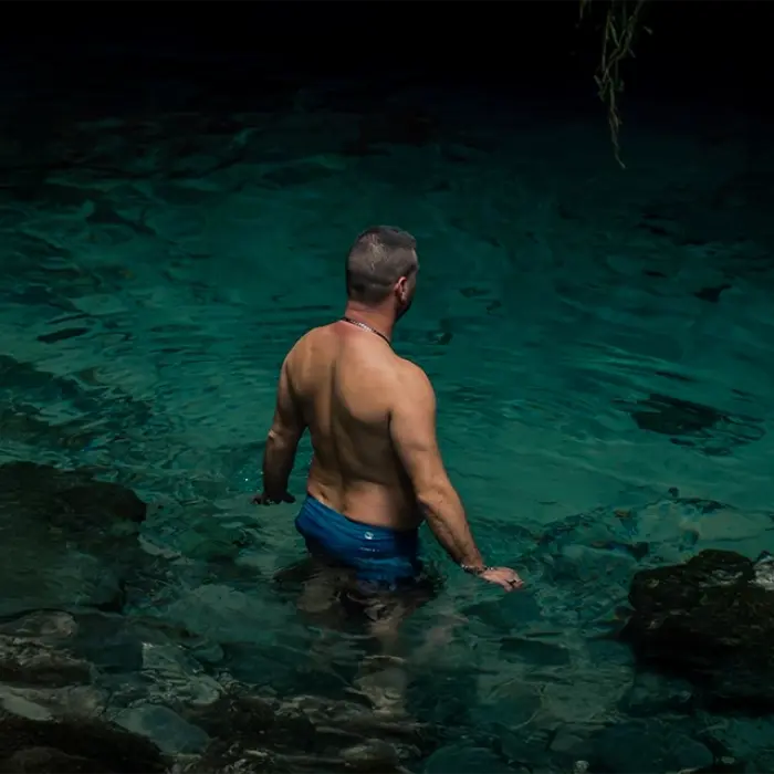 Person standing at a cenote, ready to swim in the clear water, surrounded by natural beauty in the Riviera Maya