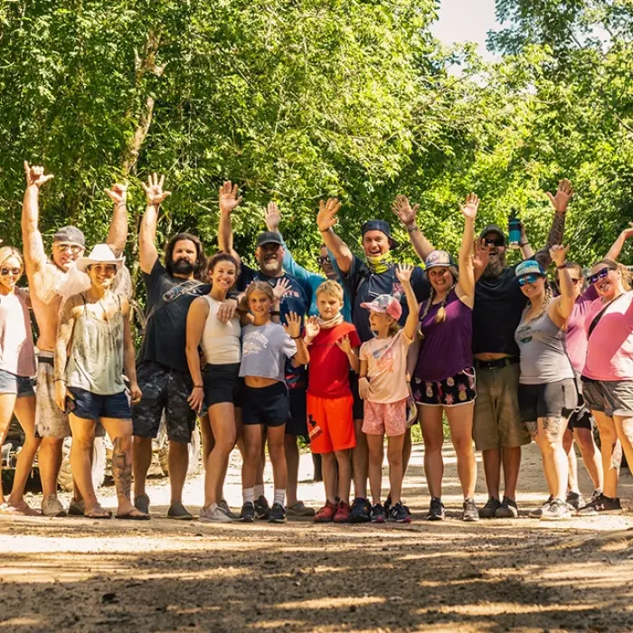 A group of people posing with their hands raised in a jungle setting during an off-road buggy tour, with ATVs and adventure vehicles in the background.
