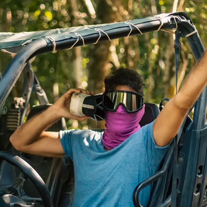 An adventure seeker inside an off-road buggy during a jungle excursion, wearing masks, sunglasses and protective gear while making thumbs-up signals